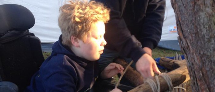 Kind in elektrische rolstoel maakt samen met begeleider een bouwwerk van touwen en hout op de regionale scoutingwedstrijden.