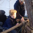 Kind in elektrische rolstoel maakt samen met begeleider een bouwwerk van touwen en hout op de regionale scoutingwedstrijden.